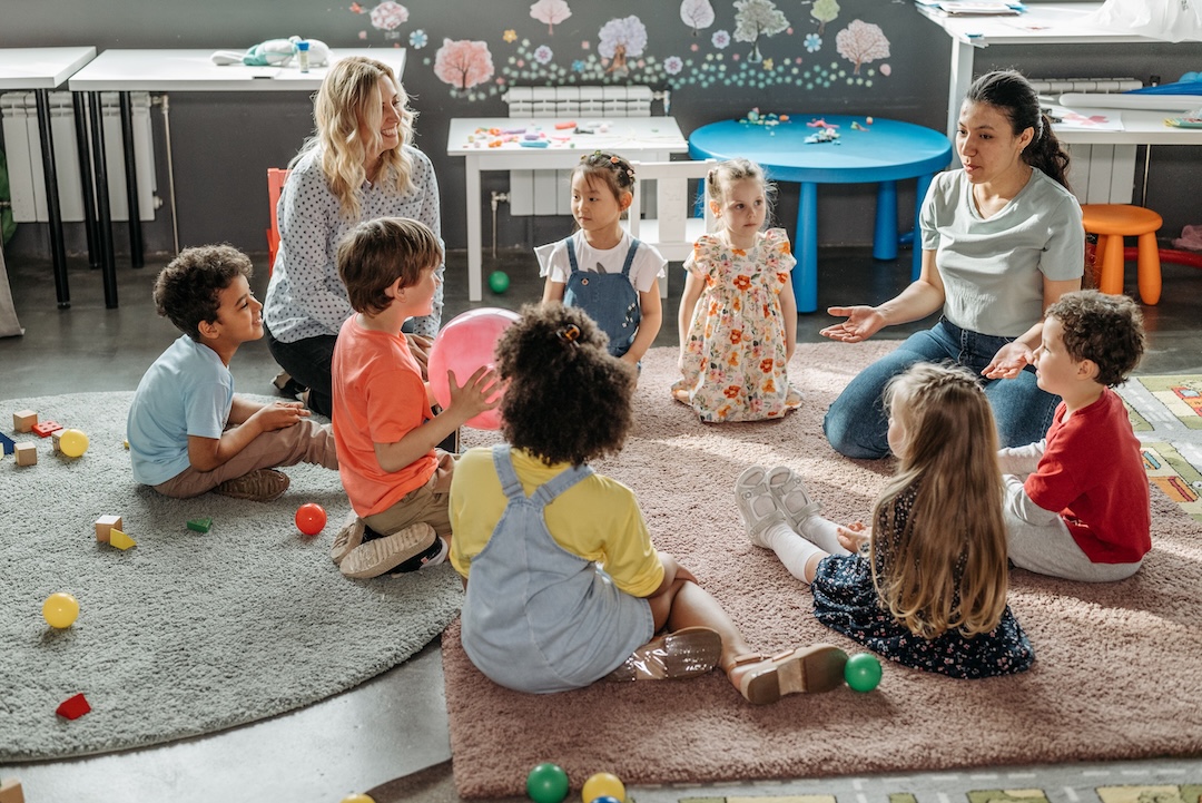 Two teachers sitting down on the floor with their students